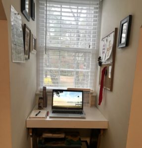A very small desk in front of a window with a laptop.